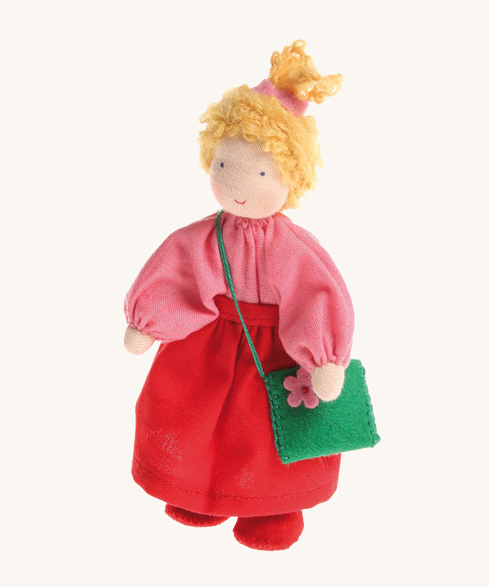 Grimm's Waldorf Blonde Girl Doll wearing a pink top, a red skirt and carrying a green felt bag with a pink flower, on a cream background