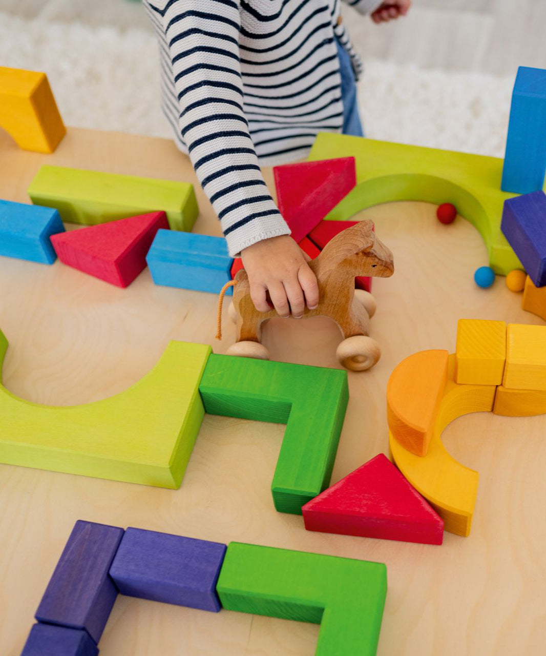 A child is pushing a wooden Grimm's horse through a maze they have created using the Grimm's Basic Building Set