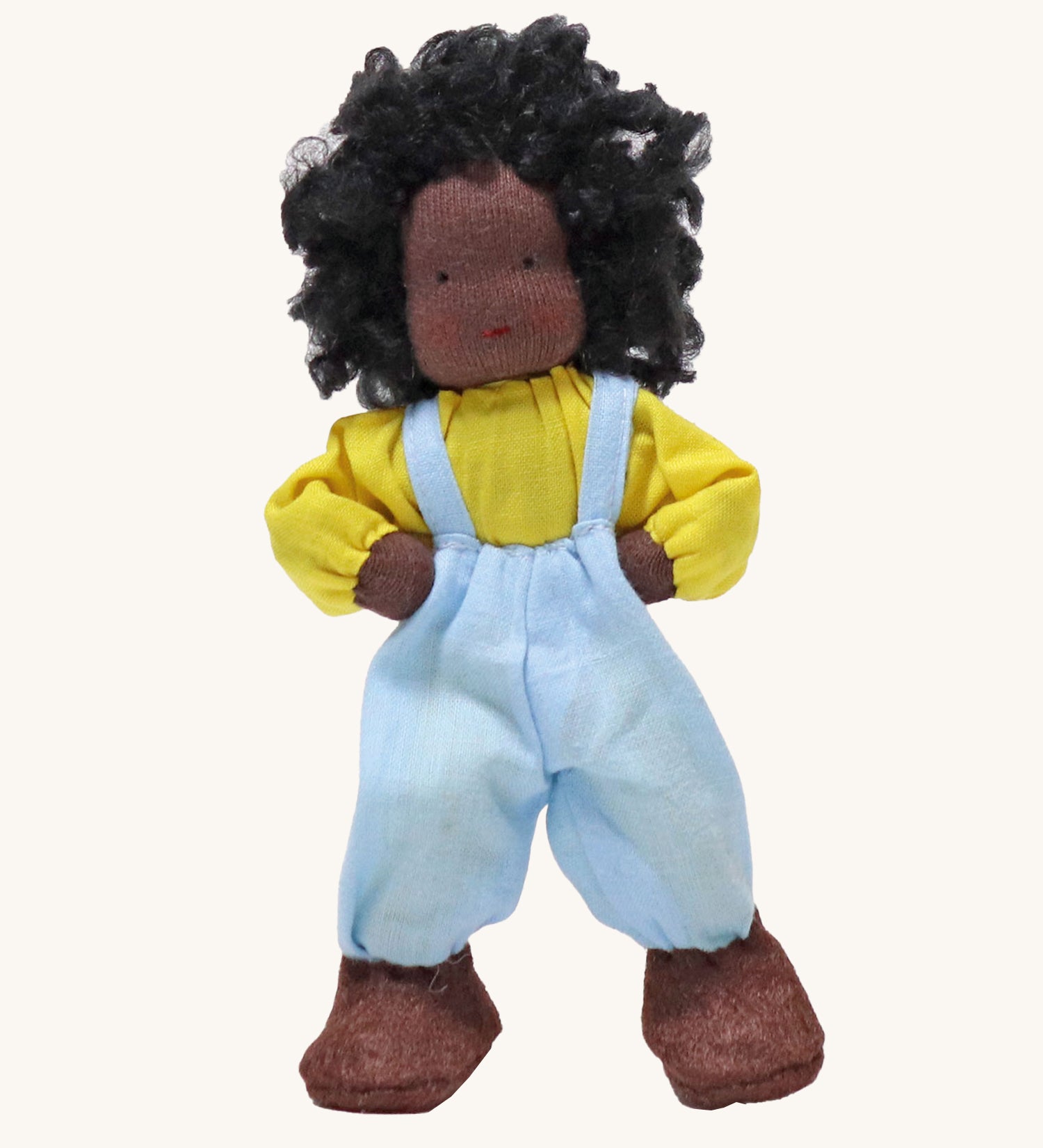 Grimm's Handmade Doll - Max is a lovely soft body doll. Max has curly black hair, black skin, a smiling face, a yellow top, light blue dungarees and brown shoes. The image is on a cream background