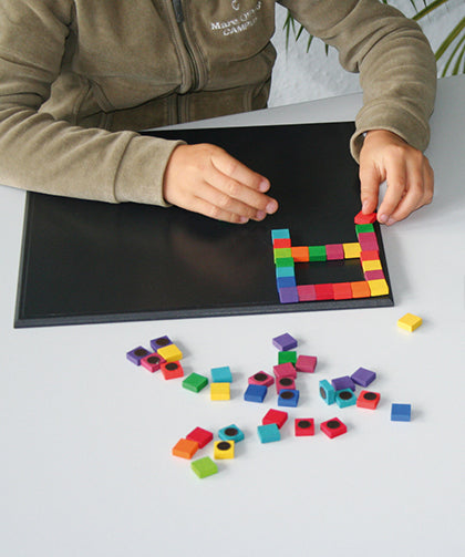 A child creating a puzzle with small magnetic blocks, using the Grimm's Small Magnetic Blackboard