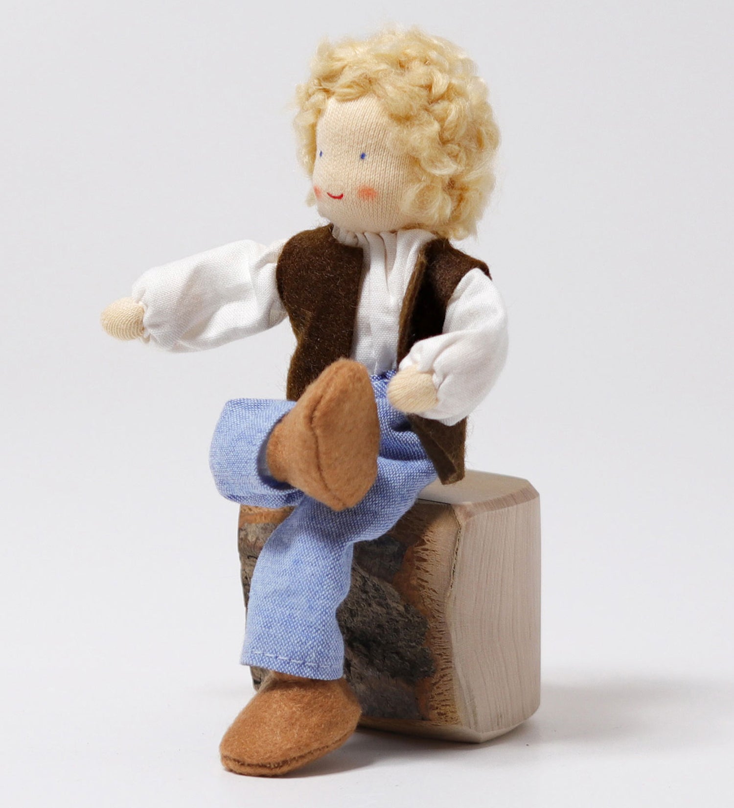 The Grimm's Blond Haired Man Doll is sat down on a block of wood with its legs crossed, showing the flexibility of the doll