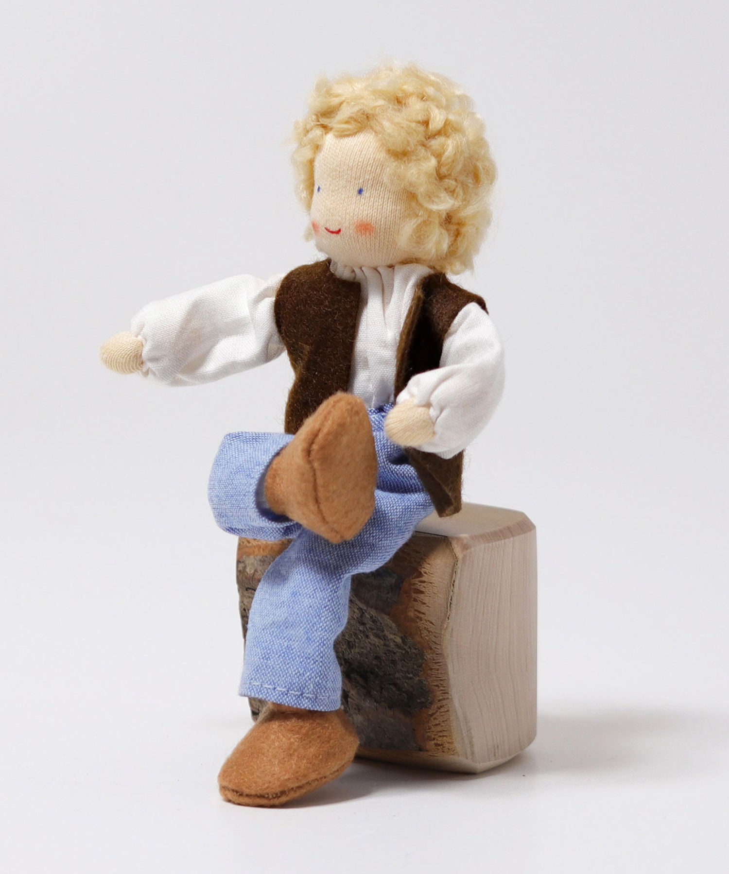 The Grimm's Blond Haired Man Doll is sat down on a block of wood with its legs crossed, showing the flexibility of the doll