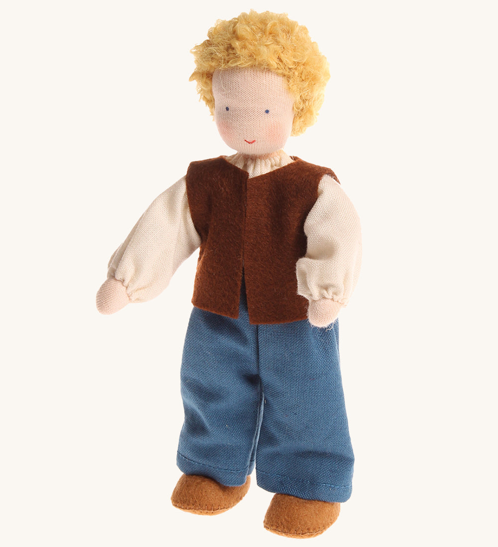 Grimm's Waldorf Blond Haired Man Doll has a soft body, blonde hair, blue eyes and is wearing light brown fabric shoes, blue trousers, a cream top and a dark brown sleeveless jacket. The image is on a cream background