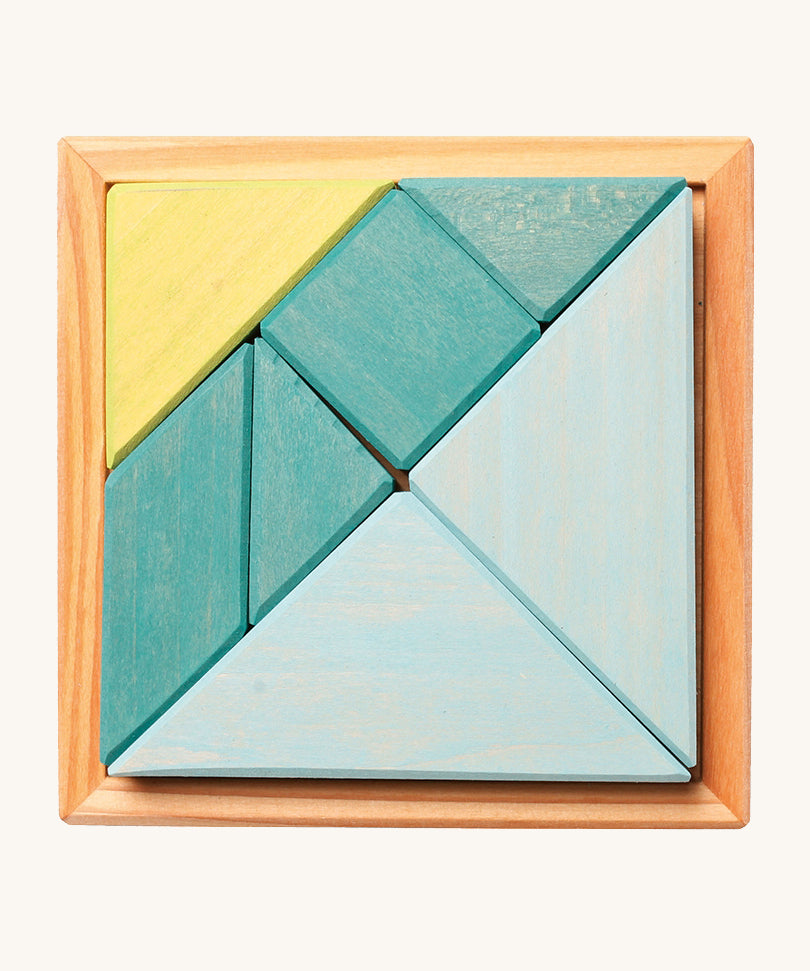 A wooden Tangram puzzle in shades of blue and green sits inside a small light wooden base on a cream background. There are 7 puzzle pieces in different shapes.