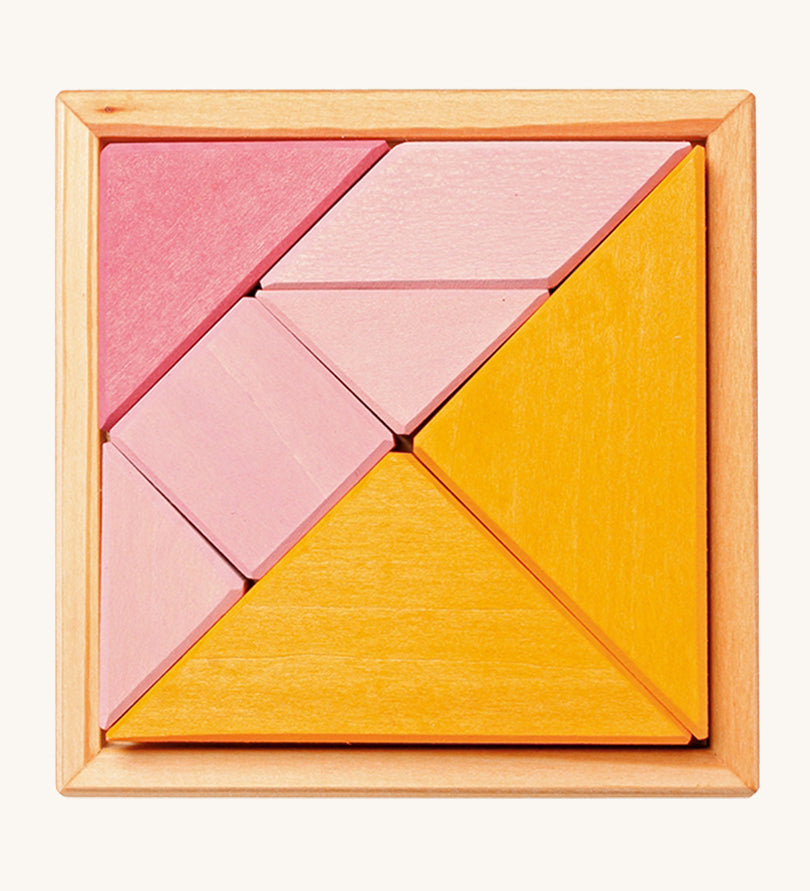 The Grimm's Tangram puzzle toy with blocks in different shapes and sizes, and colours of pink and orange sit in a small light brown wooden base on a cream background