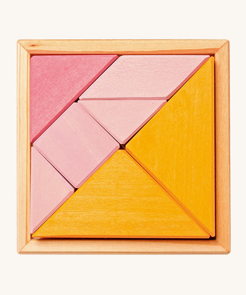 The Grimm's Tangram puzzle toy with blocks in different shapes and sizes, and colours of pink and orange sit in a small light brown wooden base on a cream background