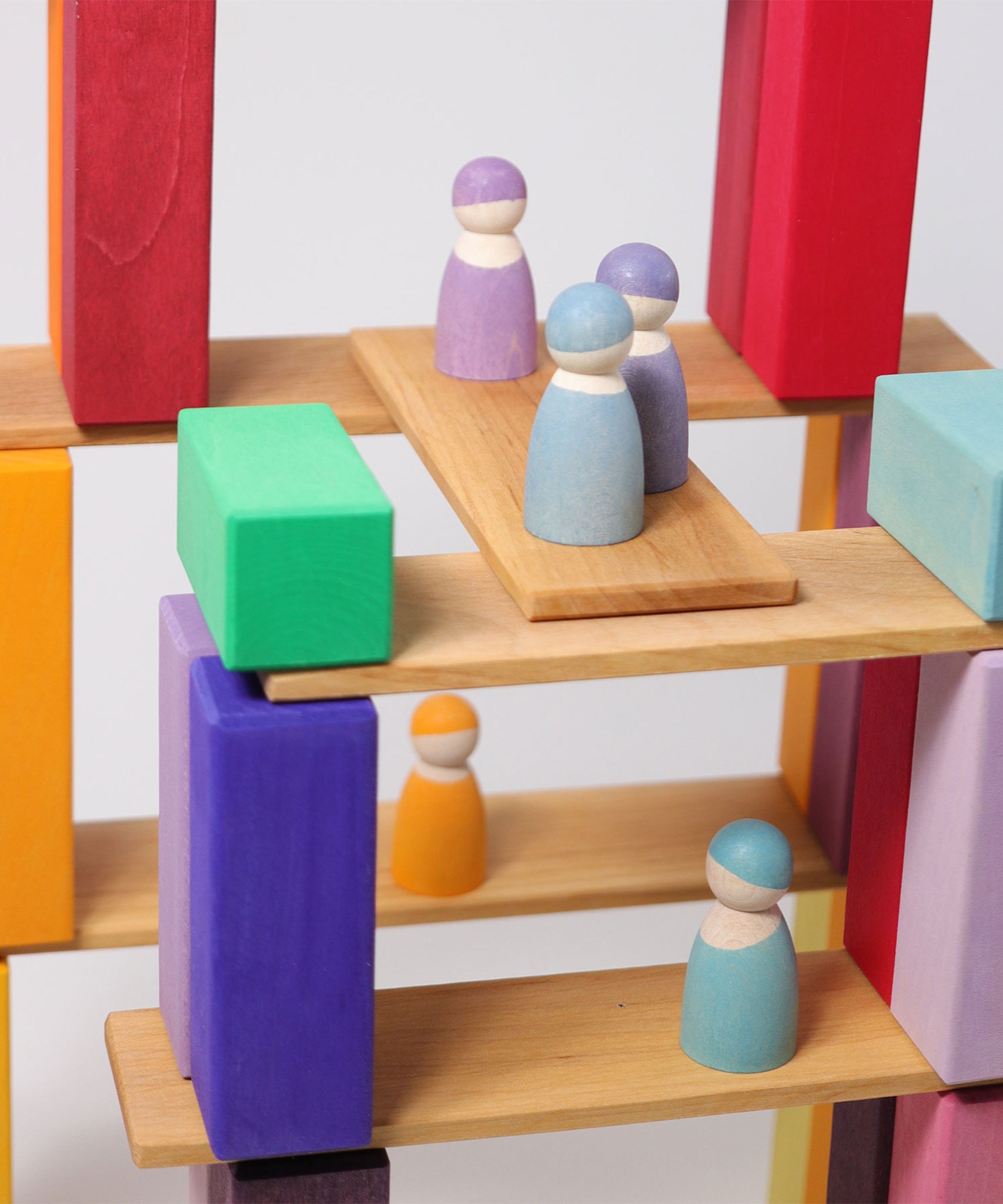 A closer view of the Grimm's 12 Pastel Friends wooden peg dolls, standing on natural wooden Grimm's building boards and colourful blocks