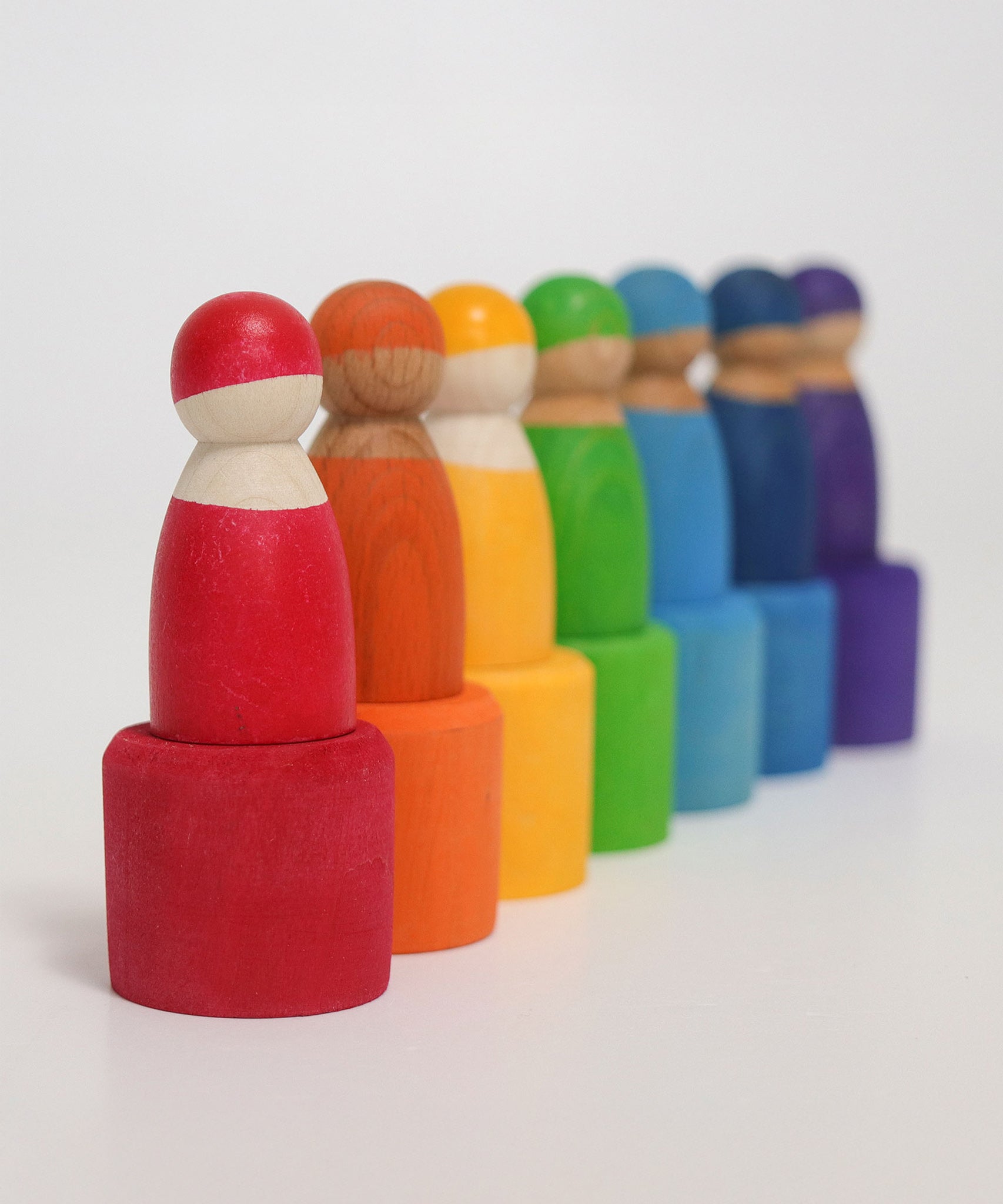 The Grimm's Rainbow Friends with bowls all lined up in a row. The wooden bowls have been turned upside down and the Grimm's Wooden Friend Dolls are stood on top