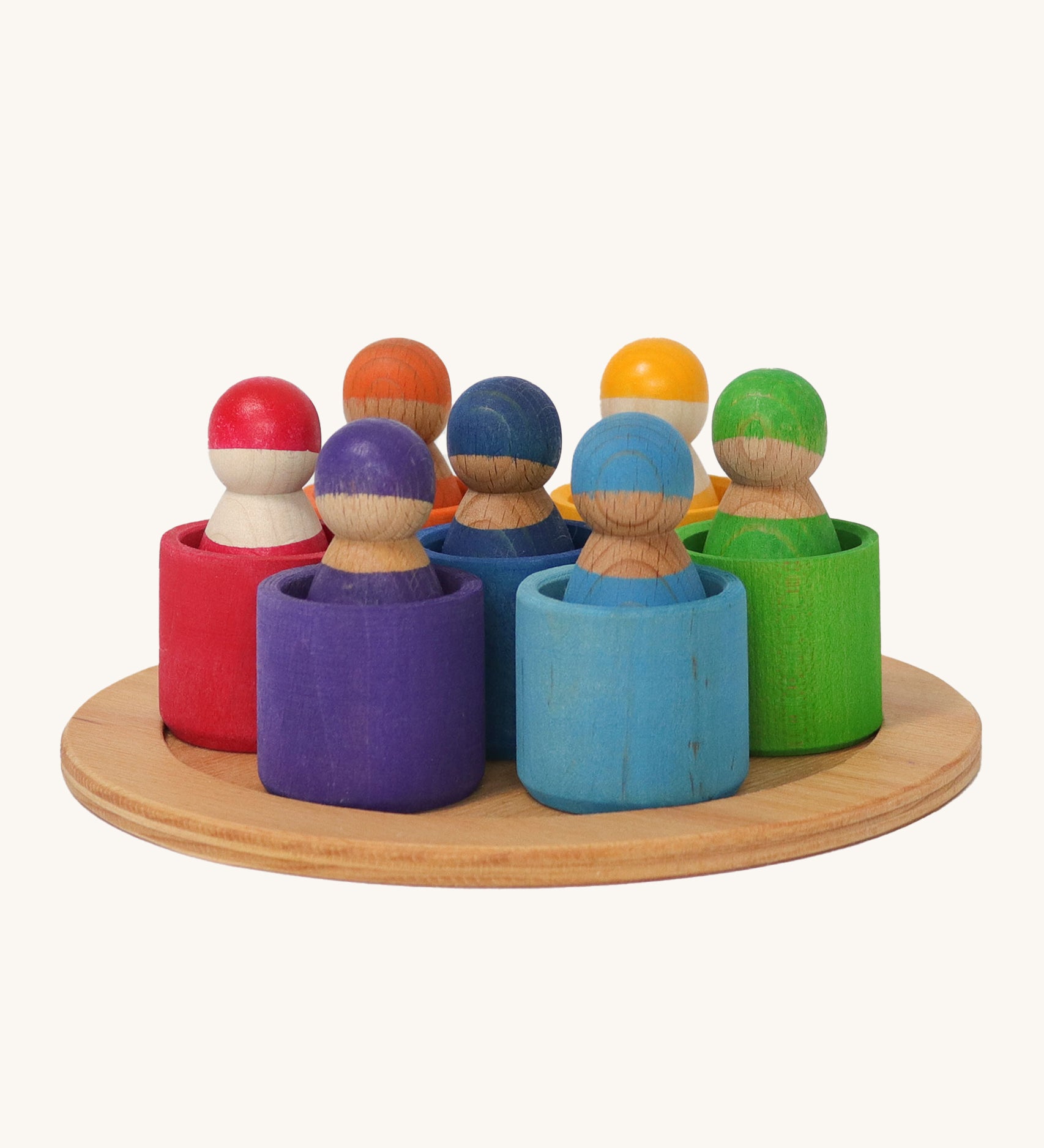 Grimm's 7 Rainbow Friends in Bowls, are an open ended, small world play toy with Grimms Friend peg dolls sat inside small wooden bowls. The Grimms Friends are removable from the bowls and can be used in open ended play. The colours of the Grimms Friends and bowls are red, purple, blue, orange, yellow, green and light blue, and are sat on a small wooden tray on a cream background.