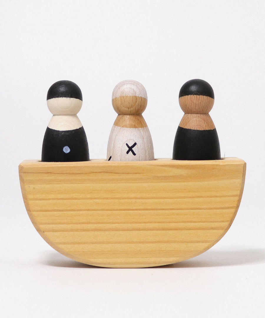 A front view of the Grimm's 3 in a Boat Monochrome kids wooden toy. The image shows the boats semi-circle shape, with the left peg dolls painted black with white spots, the middle peg doll painted white with black crosses and the left peg doll in all black