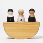 A front view of the Grimm's 3 in a Boat Monochrome kids wooden toy. The image shows the boats semi-circle shape, with the left peg dolls painted black with white spots, the middle peg doll painted white with black crosses and the left peg doll in all black