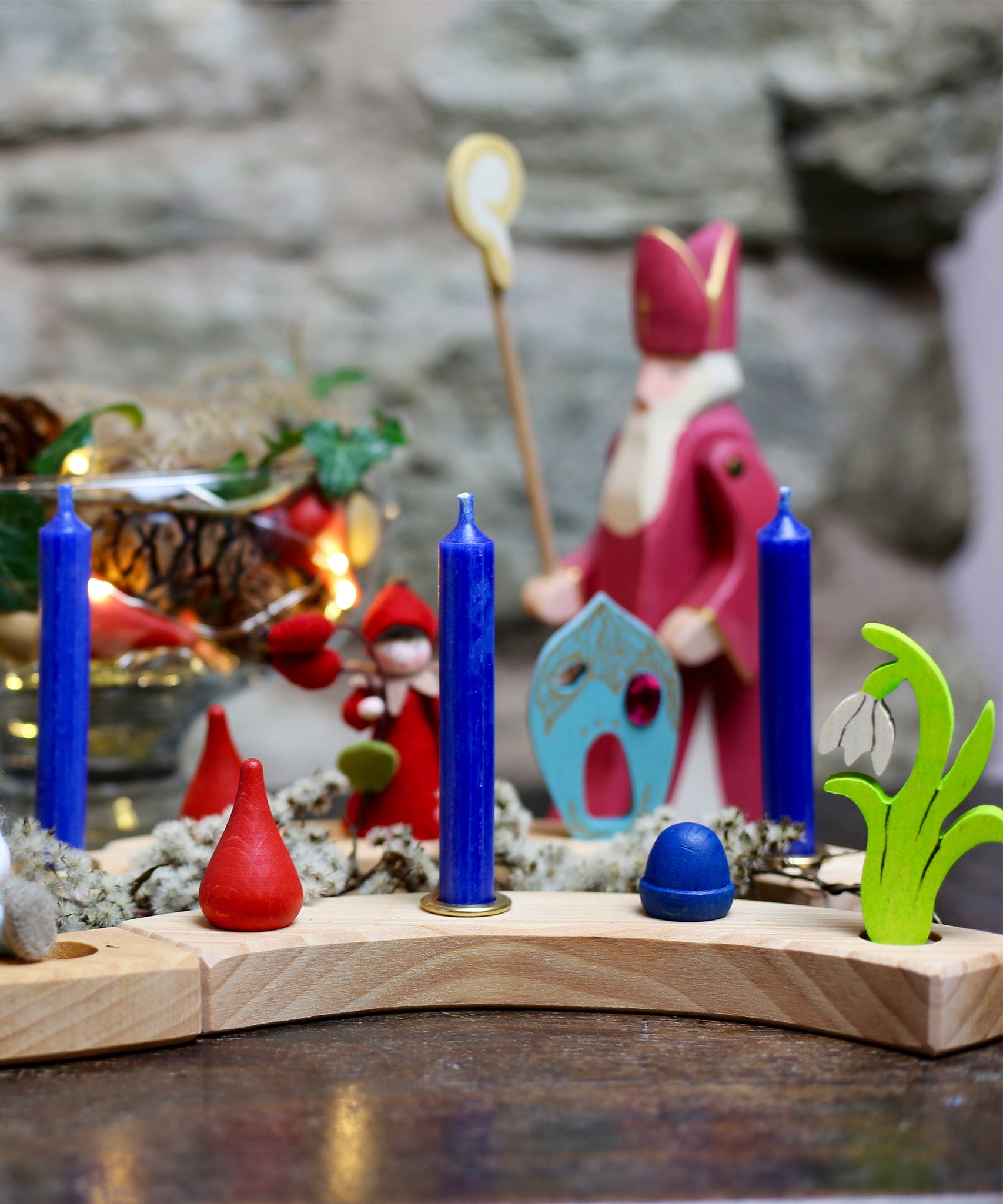 A lovely winter celebration display, made with a Grimm's Wooden Celebration ring. There are blue candles in brass holders, and colourful loose parts 