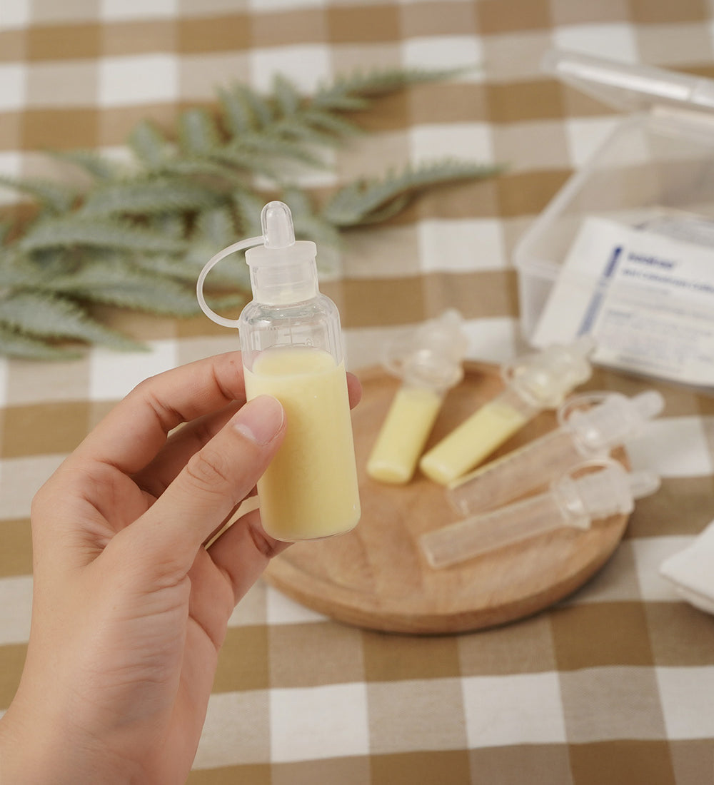 A person holding a Haakaa Silicone Colostrum Collector full of milk, in their hand with other Silicone Colostrum Collectors blurred in the background