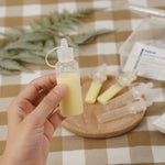 A person holding a Haakaa Silicone Colostrum Collector full of milk, in their hand with other Silicone Colostrum Collectors blurred in the background