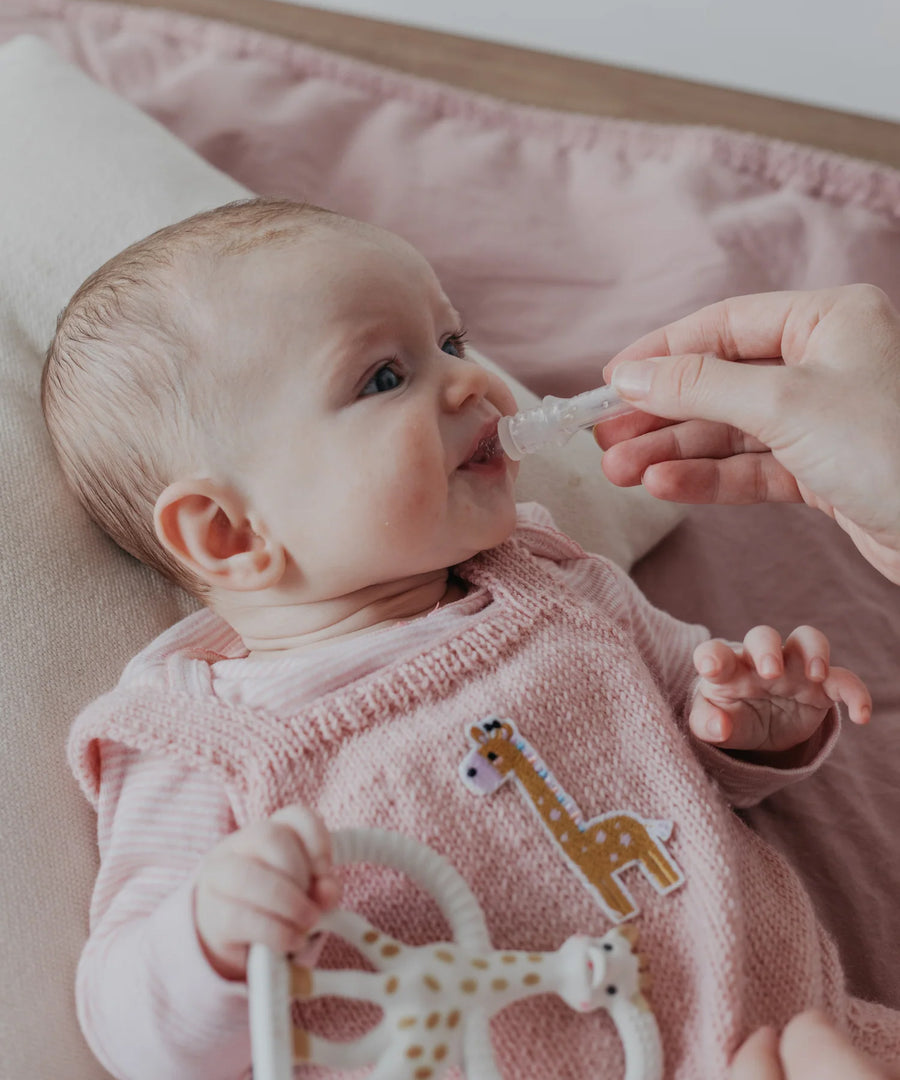 A parent using the Haakaa Silicone Colostrum Collector for their child. The child is laying down and is wearing pink clothing