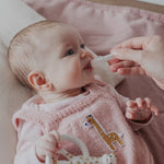 A parent using the Haakaa Silicone Colostrum Collector for their child. The child is laying down and is wearing pink clothing