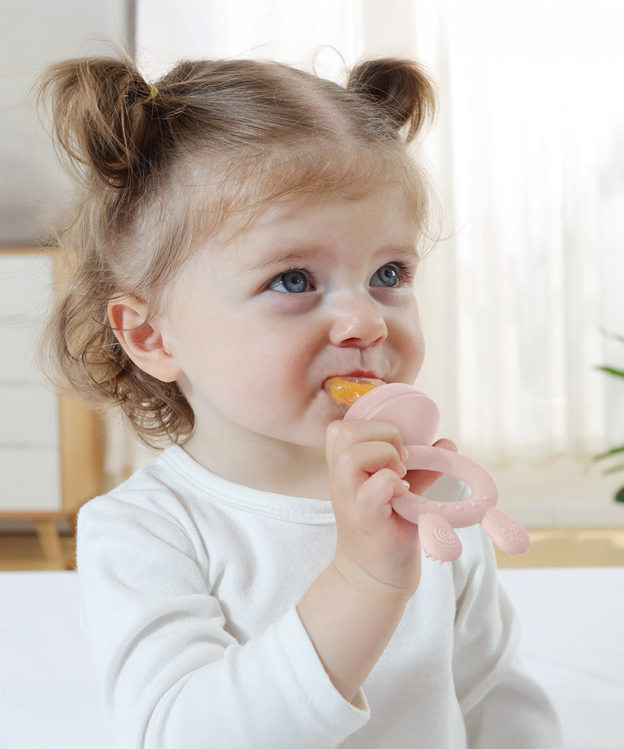 A child using the pink feeder from the Haakaa Freeze-N-Feed Mini Set. The child grasps the handle in one hand, whilst eating from the other side