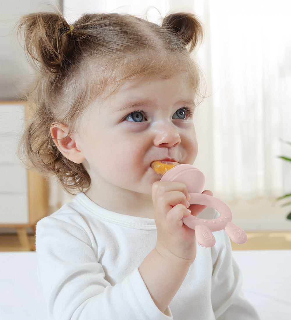 A child using the pink feeder from the Haakaa Freeze-N-Feed Mini Set. The child grasps the handle in one hand, whilst eating from the other side