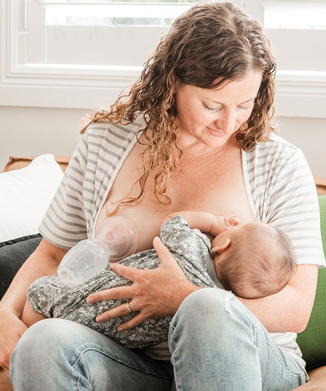 A parent breastfeeding their child, and using the Haakaa The Generation 1 100ml Silicone Breast Pump