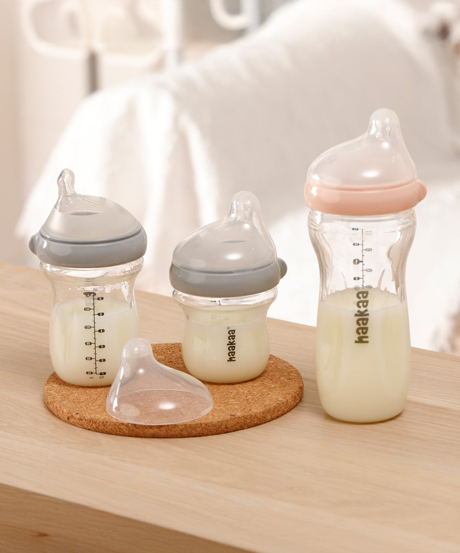 The Haakaa Generation 3 Glass Baby Bottles in 120ml /180ml/300ml, stood on a light brown table with a cork mat under 2 bottles