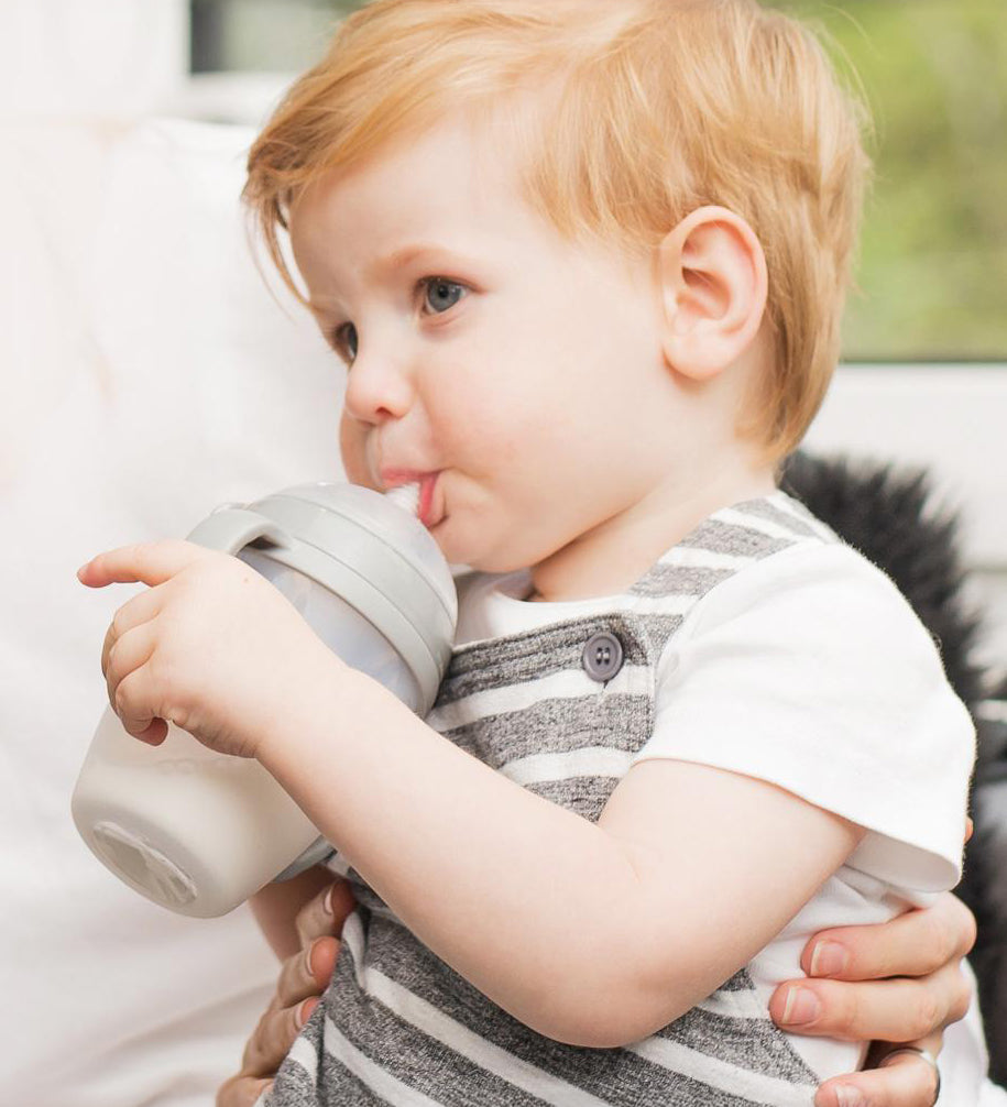 A child drinking from a Haakaa Baby Bottle, using the Generation 3 
 Silicone Bottle Handle in grey