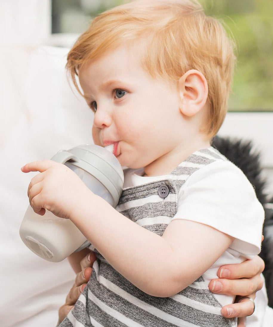 A child drinking from a Haakaa Baby Bottle, using the Generation 3 
 Silicone Bottle Handle in grey