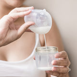 A person pouring milk from the Haakaa Ladybug Silicone Breast Milk Collector, into a Haakaa baby bottle