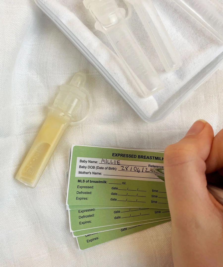 The Haakaa Silicone Colostrum Collector, with a person writing on the included green labels