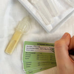 The Haakaa Silicone Colostrum Collector, with a person writing on the included green labels