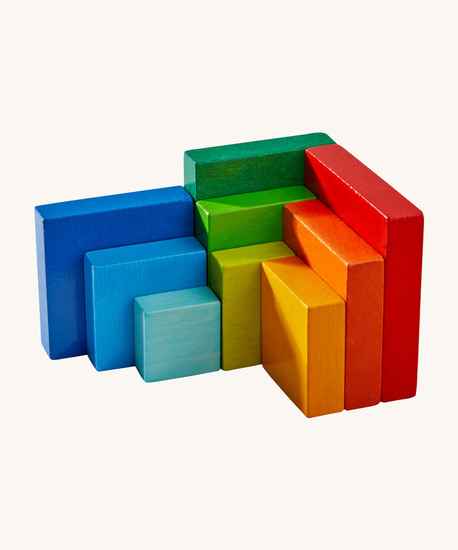 A wooden 3D Haba rainbow cube pieces lined up next to each other on a cream background.