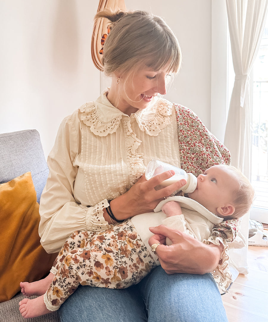 A baby feeding from the Hevea Glass Baby Bottle 120 ml on parents lap.