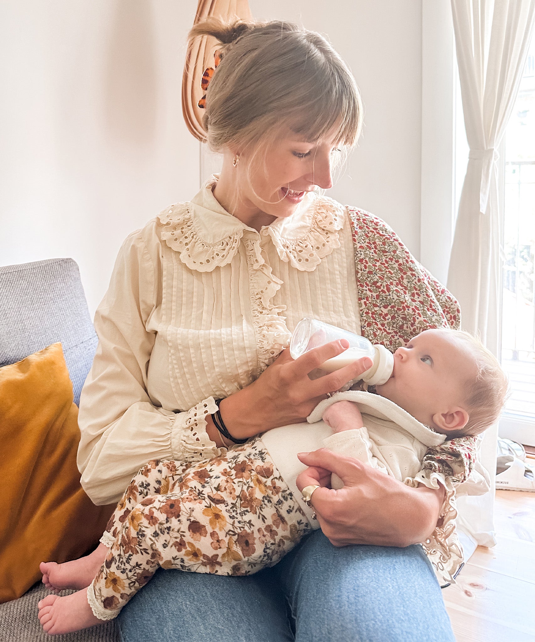 Baby feeding from a Hevea glass baby bottle on parents lap.