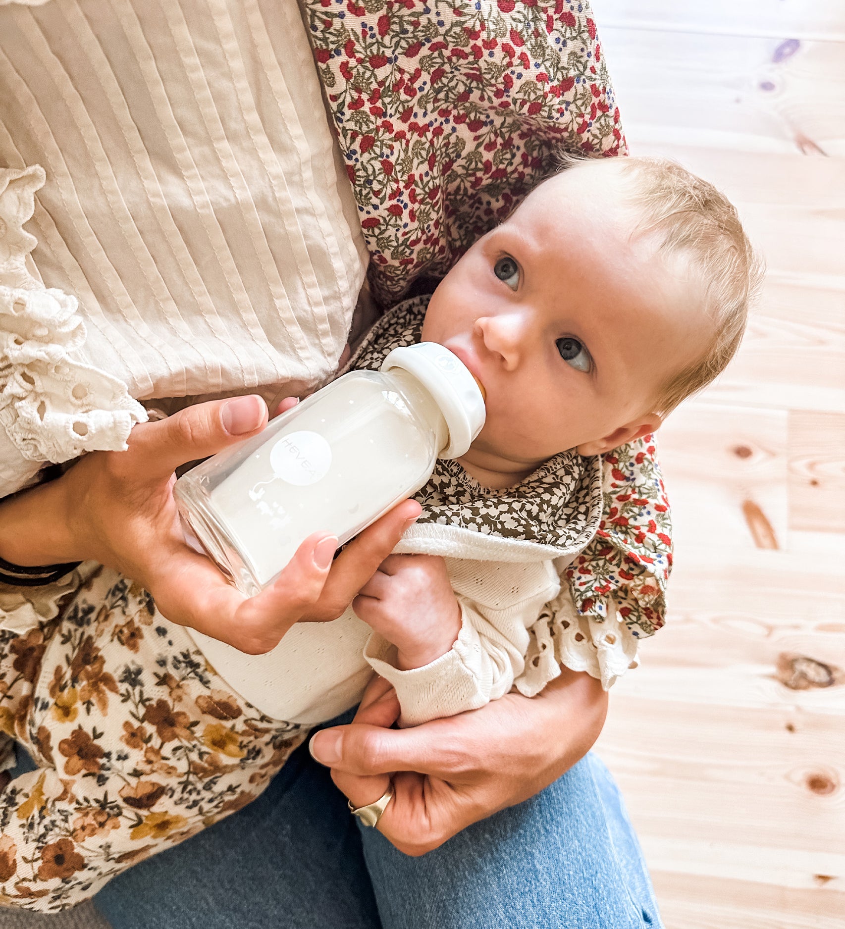 A baby feeding from the Hevea Glass Baby Bottle 120 ml on parents lap.