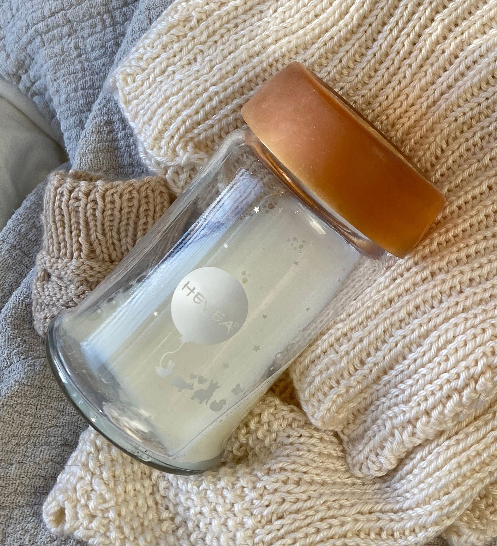 Hevea Wide Neck Glass Baby Bottle with Natural Rubber Cap on a white knitted blanket. 