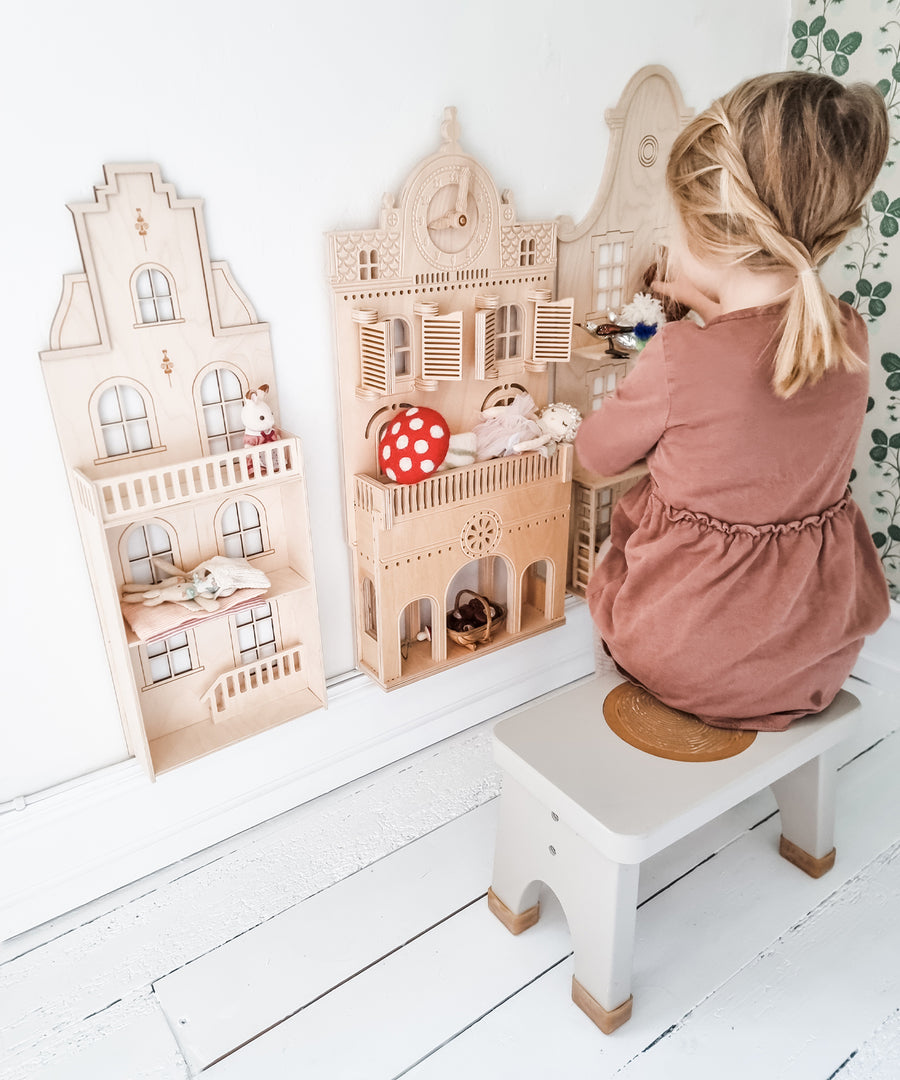 Child in a pink dress sat on a Hevea Rubberwood Step Stool, playing with a dolls house.