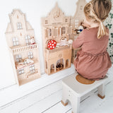 Child in a pink dress sat on a Hevea Rubberwood Step Stool, playing with a dolls house.