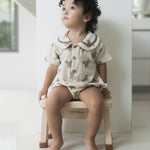 Child in a white romper sat on a Hevea Rubberwood Step Stool.