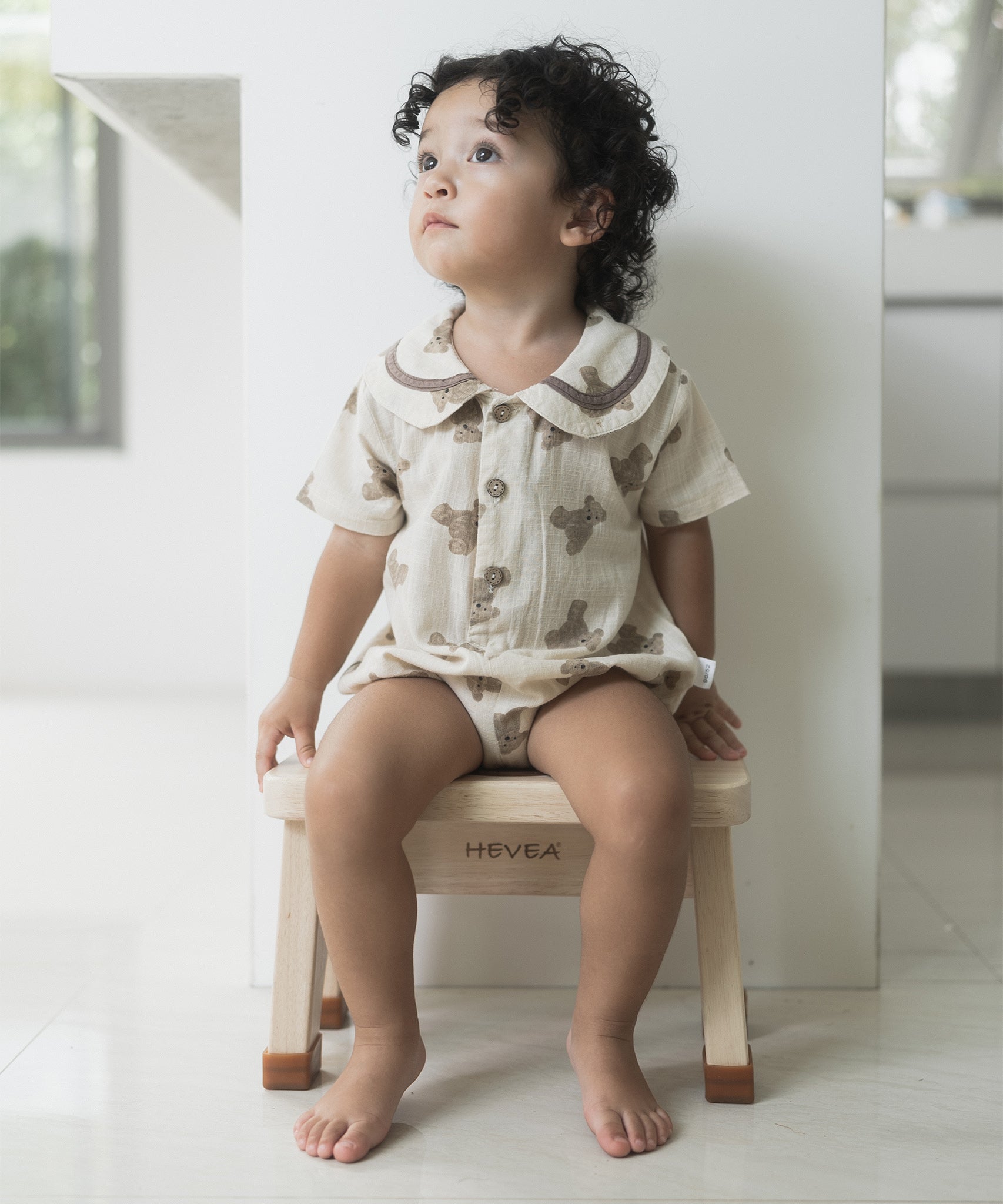 Child in a white romper sat on a Hevea Rubberwood Step Stool.