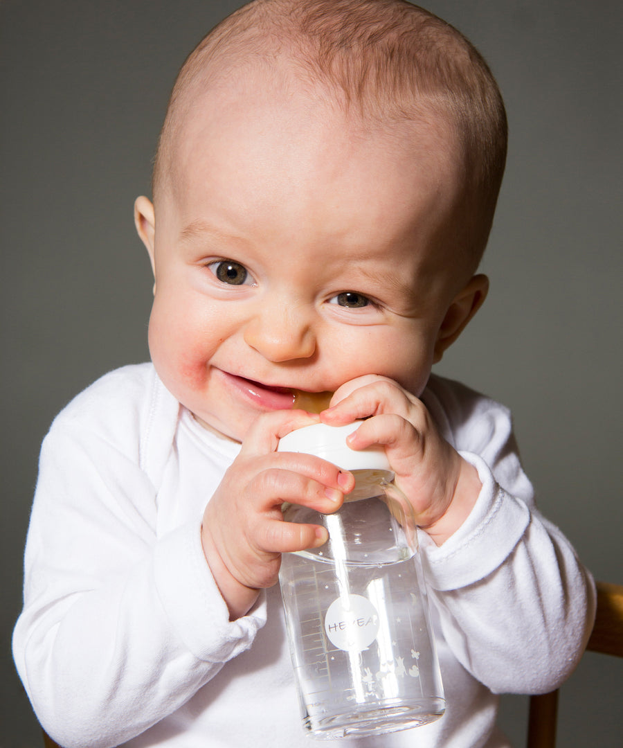 Baby biting down on a 100% natural rubber bottle nipple by HEVEA.