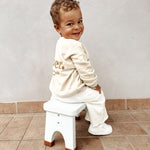 Child in a white tracksuit sat on a Hevea Rubberwood Step Stool.