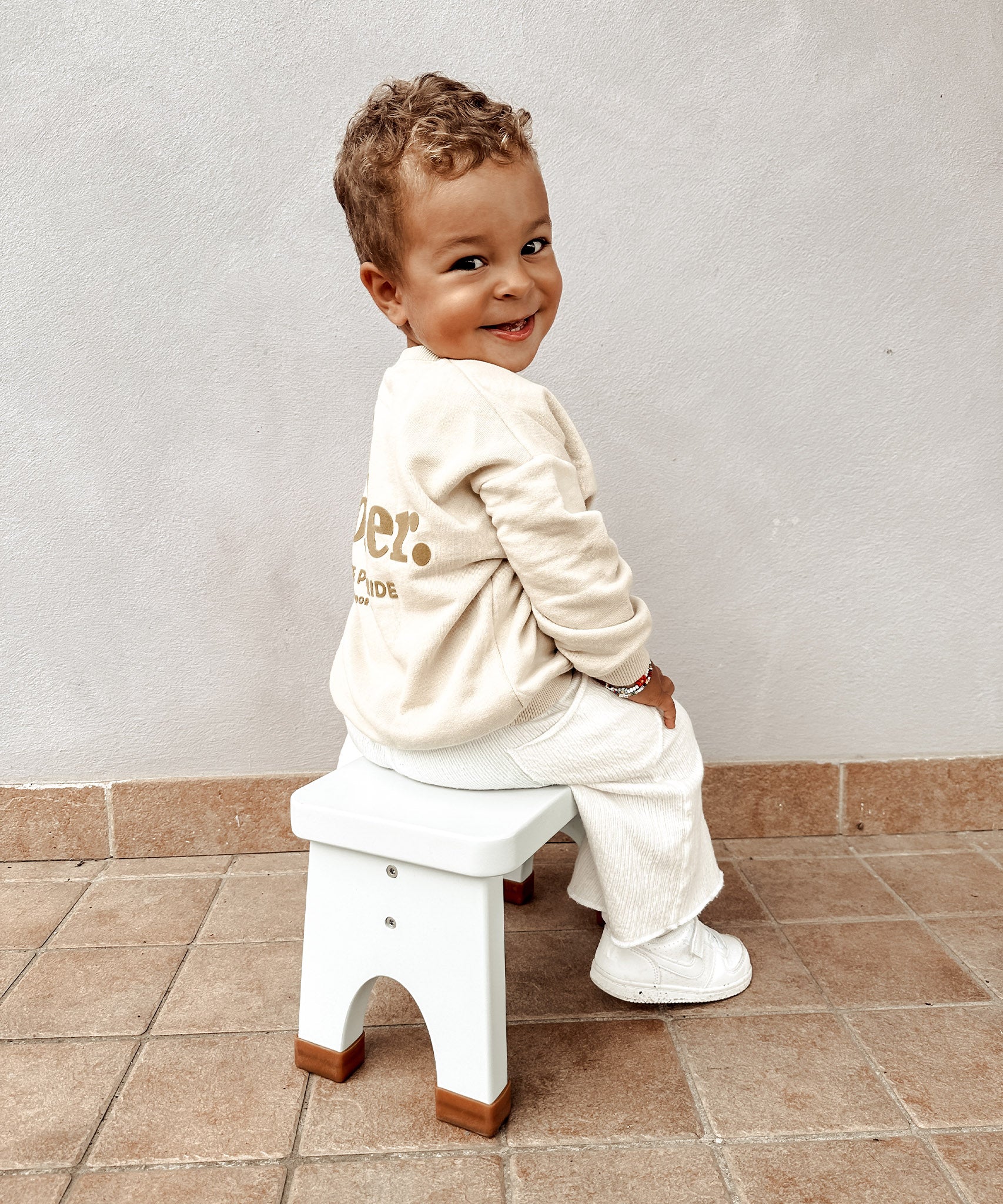 Child in a white tracksuit sat on a Hevea Rubberwood Step Stool.