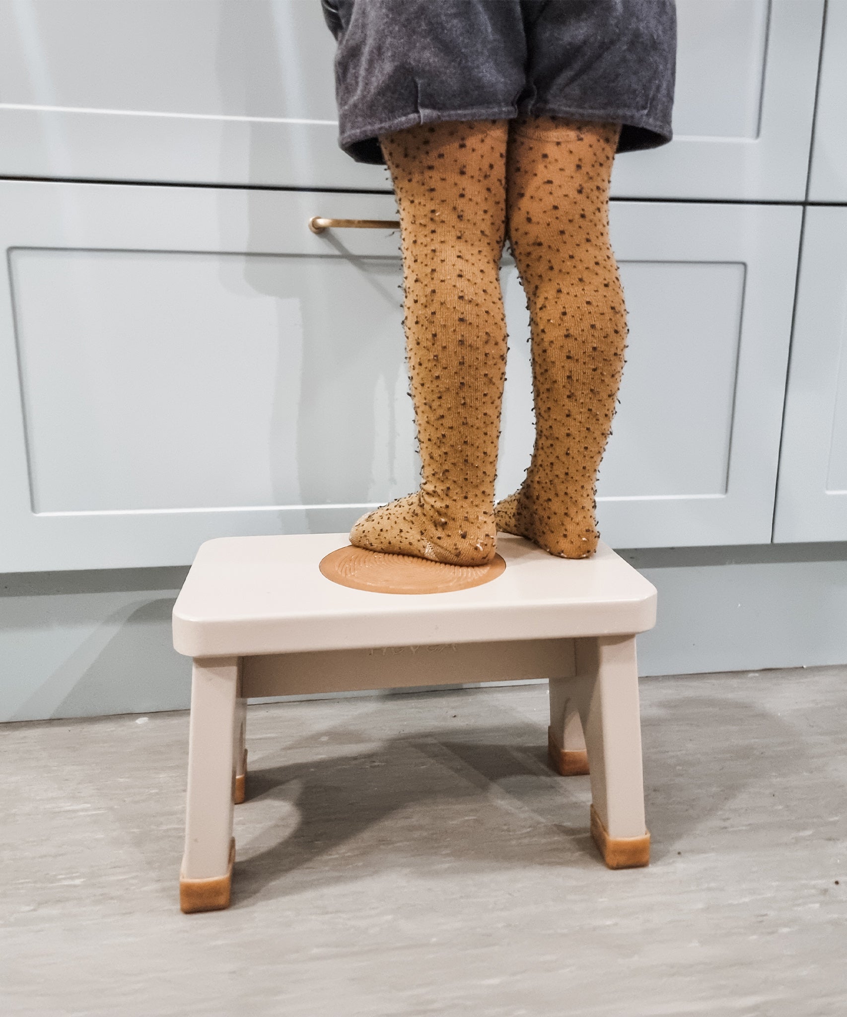 Child in yellow tights stood on a Hevea Rubberwood Step Stool at a kitchen counter. 