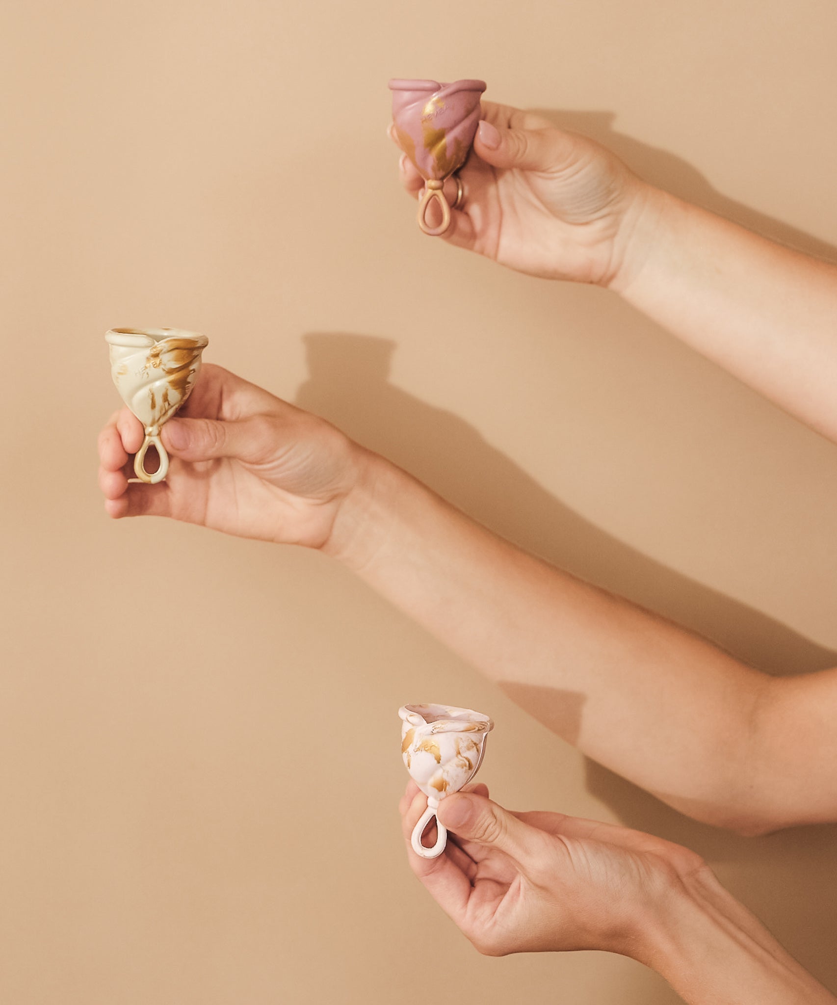 Three sizes of Hevea LOOP menstrual cups being held up.