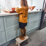 Child in yellow tights preparing food stood on a Hevea Rubberwood Step Stool at a kitchen counter.