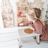 Child in a pink dress sat on a Hevea Rubberwood Step Stool, playing with a dolls house.