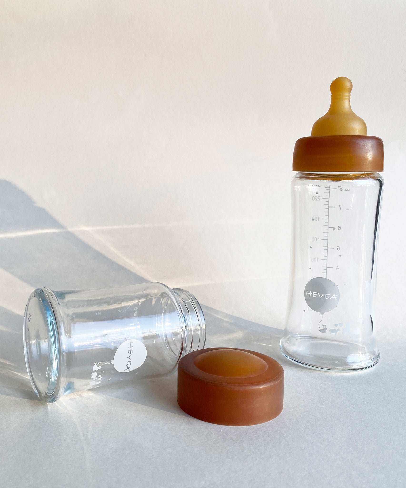 Hevea Wide Neck Glass Baby Bottle Natural Rubber Cap next to a glass baby bottle.