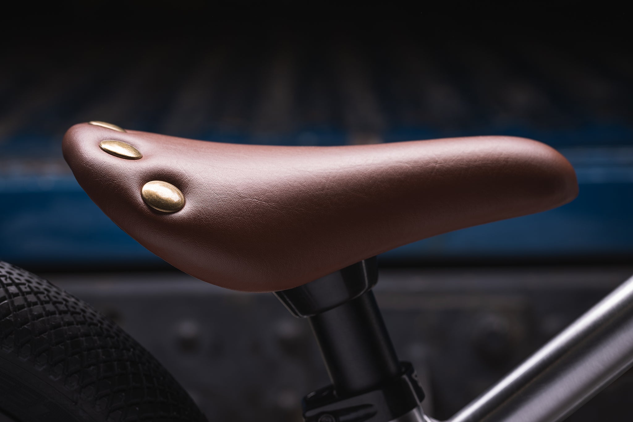 The Early Rider Charger Balance Bike adjustable seat, in a tan brown colour and gold flat rivets on the back of the seat