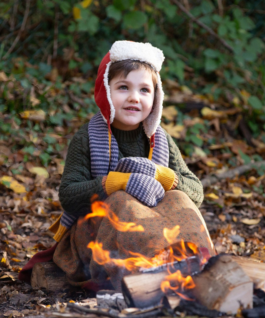 A child outside in the woods, snuggled under and comfy blanket wearing the Dreamy Blue Striped Knitted Mittens