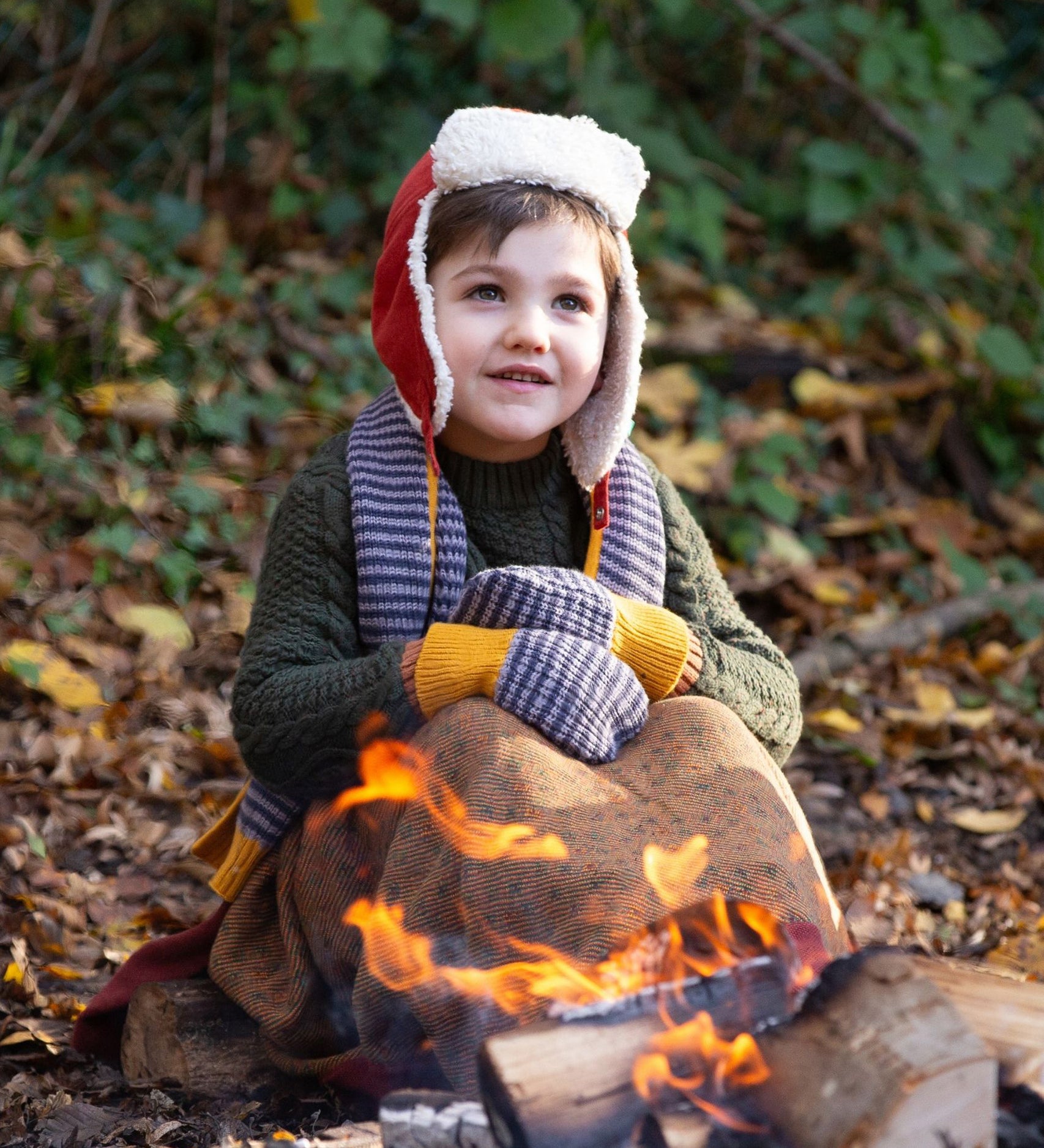 A child outside in the woods, snuggled under and comfy blanket wearing the Dreamy Blue Striped Knitted Mittens