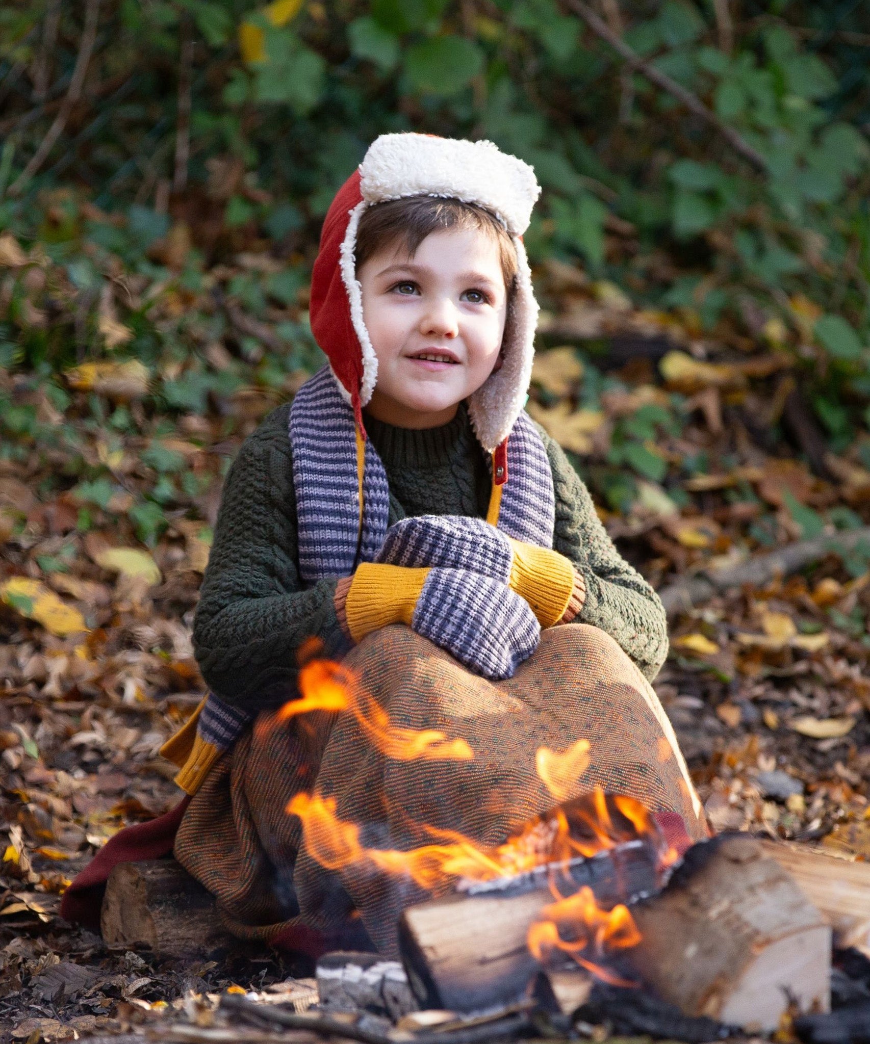 A child outside in the woods, snuggled under and comfy blanket wearing the Dreamy Blue Striped Knitted Mittens